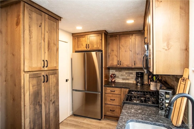 kitchen featuring sink, stainless steel appliances, light hardwood / wood-style flooring, backsplash, and a textured ceiling