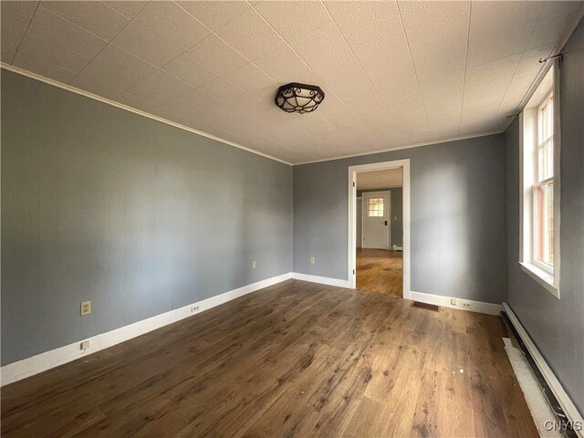 unfurnished room with wood-type flooring, a baseboard radiator, a wealth of natural light, and ornamental molding