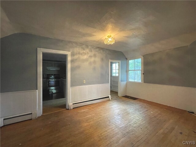 empty room with hardwood / wood-style flooring, vaulted ceiling, and baseboard heating