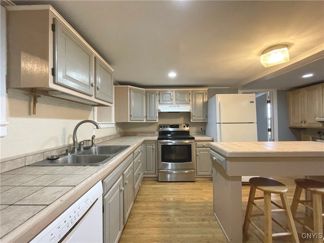 kitchen with tile counters, white appliances, sink, and light hardwood / wood-style flooring