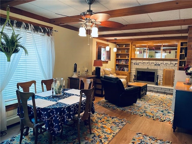 dining space with ceiling fan, a brick fireplace, plenty of natural light, and wood-type flooring