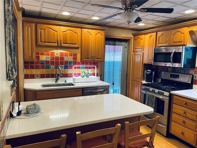 kitchen featuring light wood-type flooring, ceiling fan, sink, stainless steel appliances, and backsplash