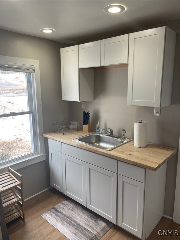 kitchen featuring sink, butcher block countertops, hardwood / wood-style flooring, and white cabinetry