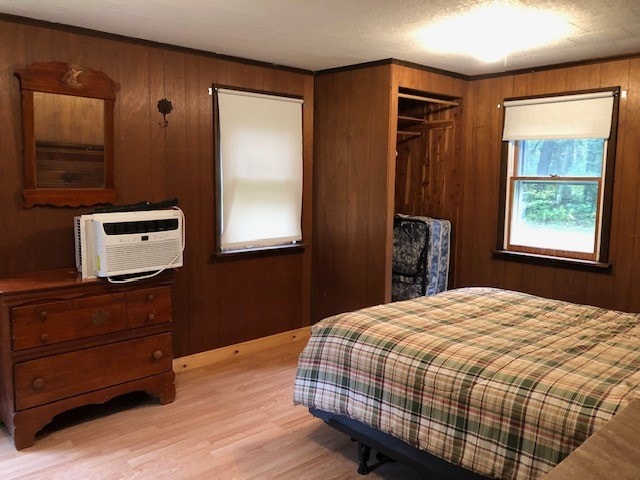 bedroom with a textured ceiling, light wood-type flooring, wood walls, and a wall unit AC