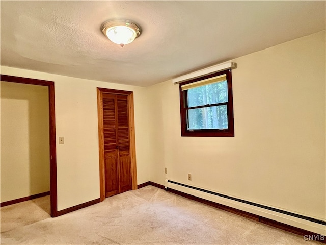 unfurnished bedroom featuring light carpet, a closet, a baseboard heating unit, and a textured ceiling