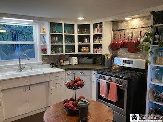 kitchen with stainless steel gas range, sink, and white cabinets