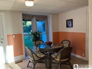 carpeted dining area with a paneled ceiling