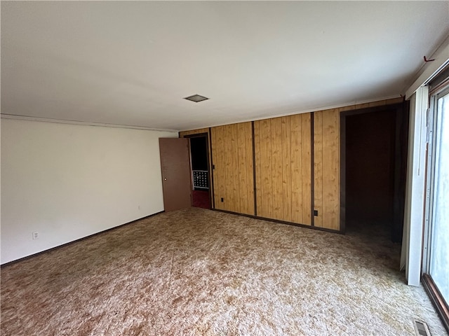 unfurnished bedroom with light carpet, a closet, and wood walls