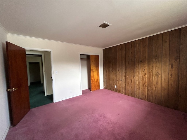 unfurnished bedroom featuring crown molding, a closet, wood walls, and carpet