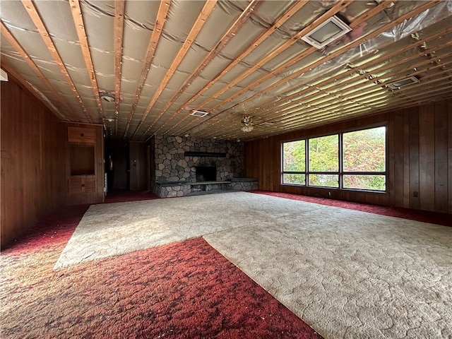 unfurnished living room featuring ceiling fan, a fireplace, wood walls, and carpet