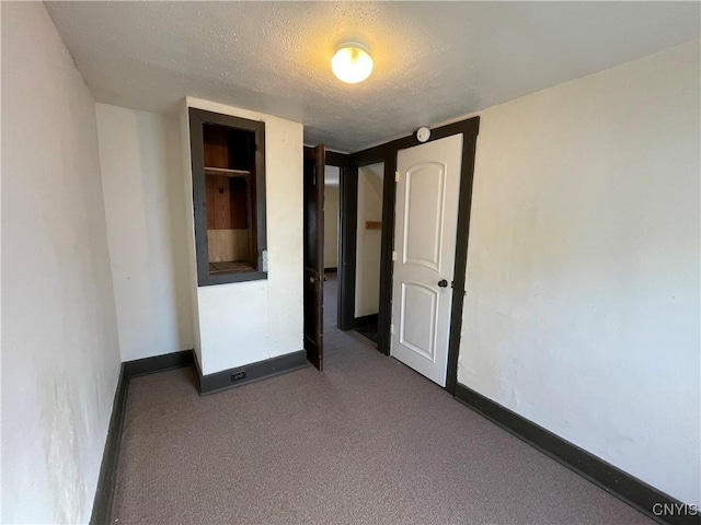 unfurnished bedroom with a textured ceiling and dark carpet