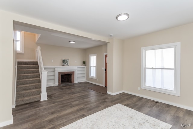 unfurnished living room with a brick fireplace, dark hardwood / wood-style floors, and a healthy amount of sunlight