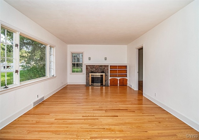 unfurnished living room with light wood-type flooring and a stone fireplace