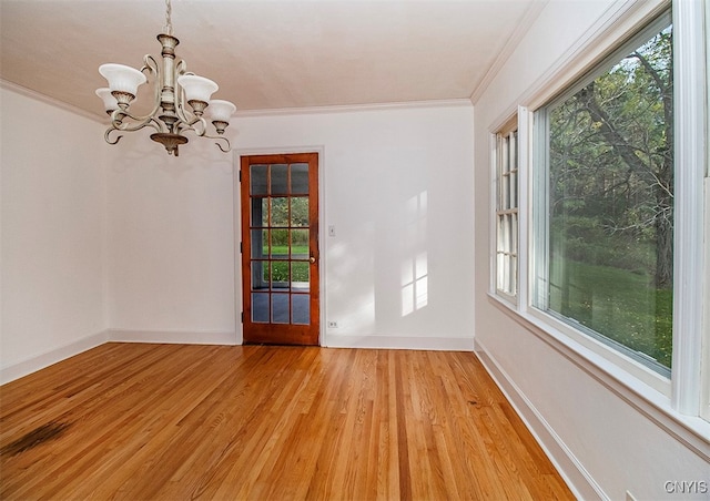 empty room with a notable chandelier, plenty of natural light, light hardwood / wood-style floors, and crown molding