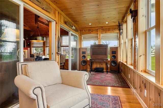 living area featuring wood walls, light wood-type flooring, wooden ceiling, and a healthy amount of sunlight