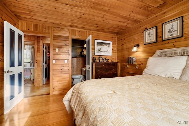 bedroom with ensuite bathroom, wooden walls, light wood-type flooring, and wood ceiling