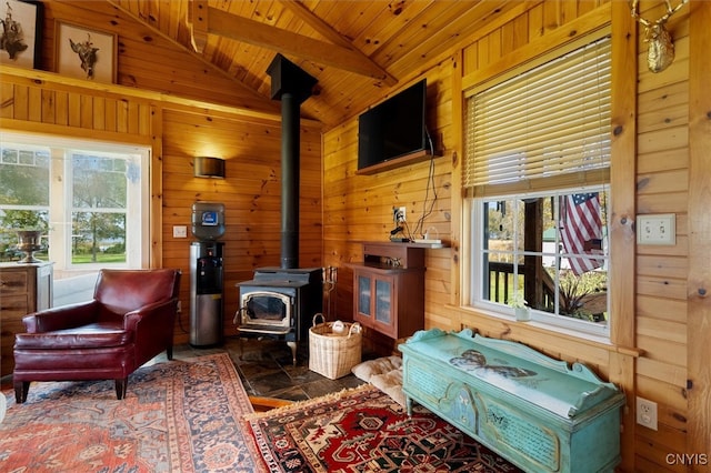 living room with lofted ceiling with beams, wood walls, a wood stove, and a healthy amount of sunlight