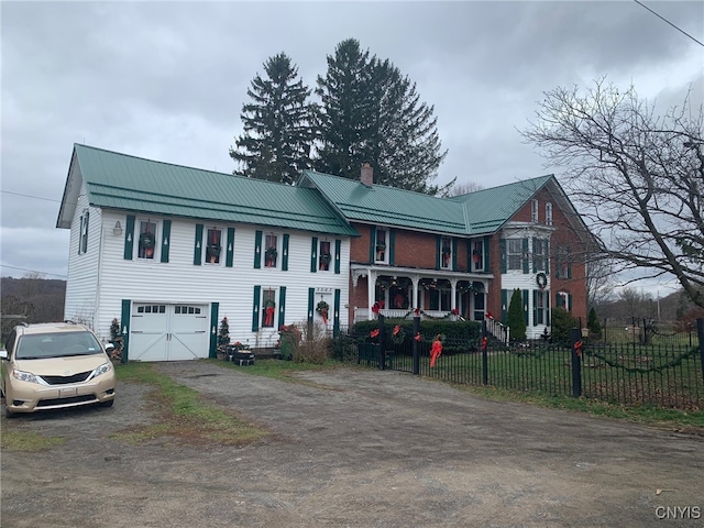 view of front facade featuring metal roof, a fenced front yard, an attached garage, dirt driveway, and a chimney