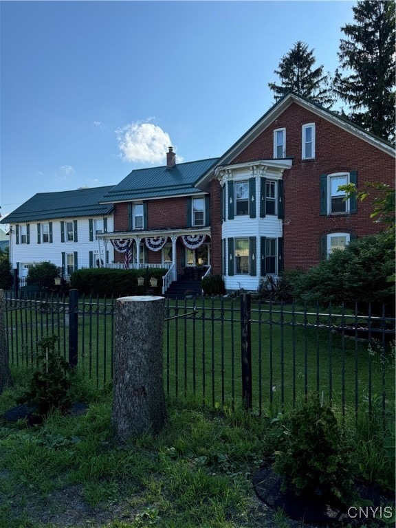 view of front of property with metal roof, a fenced front yard, brick siding, a chimney, and a front yard