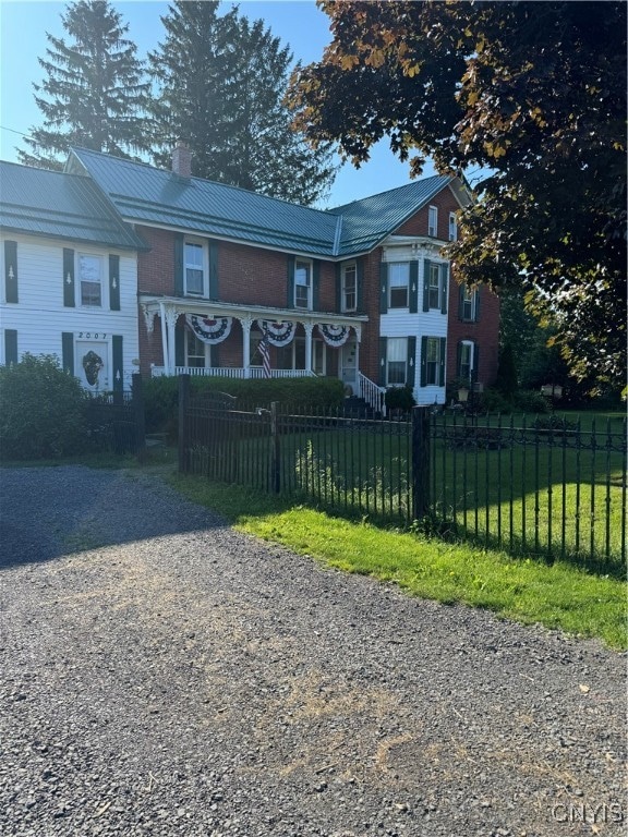 view of front facade featuring metal roof, a fenced front yard, brick siding, a chimney, and gravel driveway