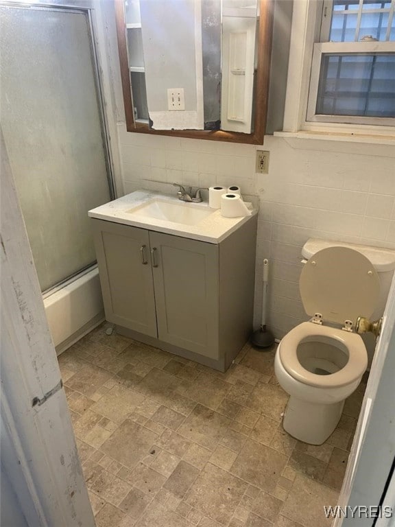 full bathroom with vanity, toilet, shower / bath combination with glass door, and tile walls