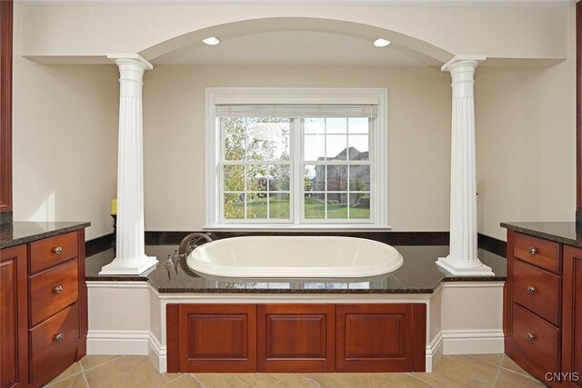 bathroom with tile patterned floors, a tub to relax in, vanity, and ornate columns