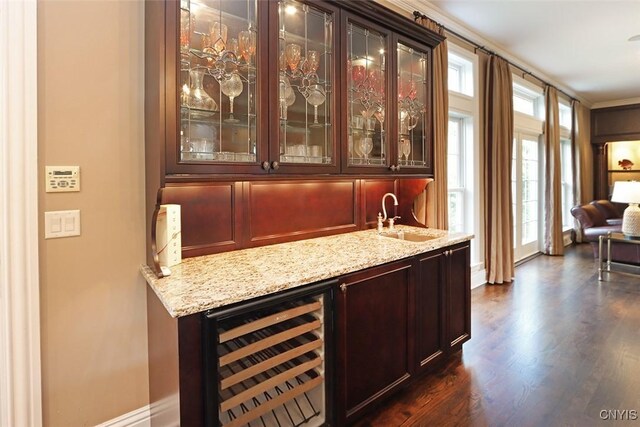 bar with dark hardwood / wood-style floors, beverage cooler, light stone counters, and sink