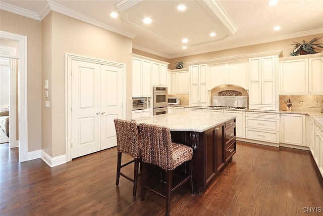 kitchen featuring a breakfast bar area, decorative backsplash, dark wood-type flooring, a kitchen island, and light stone counters