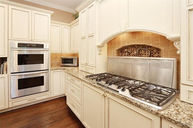 kitchen with stainless steel appliances, tasteful backsplash, dark hardwood / wood-style floors, light stone counters, and crown molding