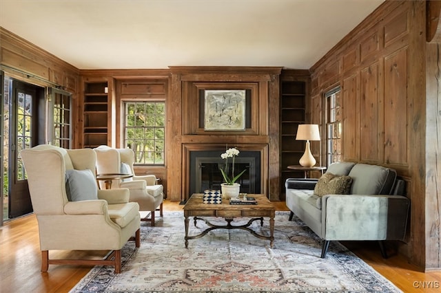 living area with wooden walls, built in shelves, and light hardwood / wood-style floors