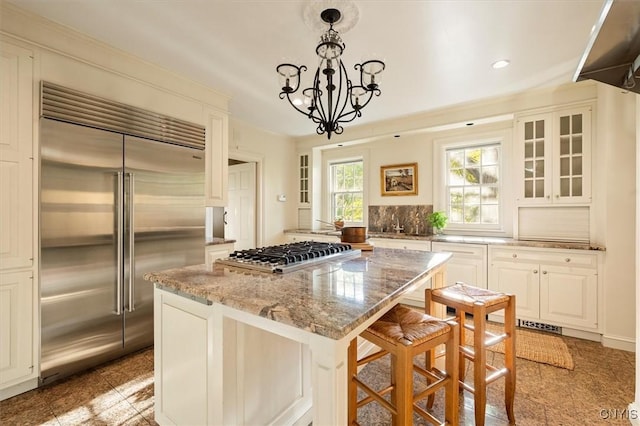 kitchen with an inviting chandelier, light stone countertops, a center island, glass insert cabinets, and appliances with stainless steel finishes
