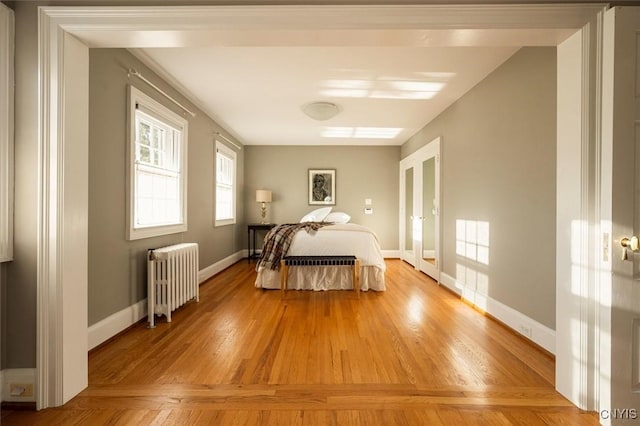 bedroom featuring radiator heating unit, baseboards, light wood-style flooring, and french doors
