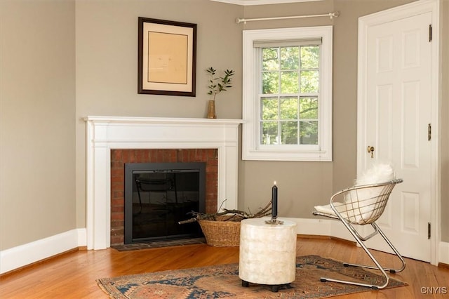 sitting room with baseboards, a brick fireplace, and wood finished floors