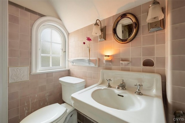 half bath with tile walls, vaulted ceiling, a sink, and toilet