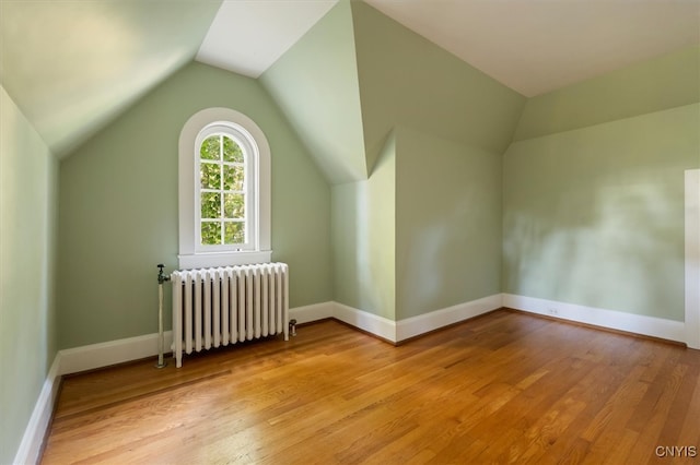 additional living space with lofted ceiling, radiator heating unit, and light wood-type flooring