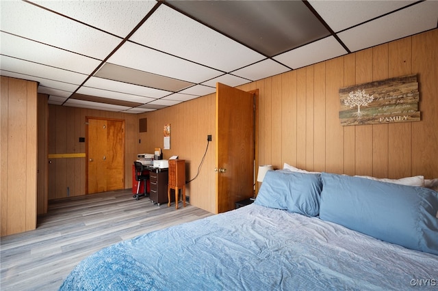 bedroom featuring wooden walls, a drop ceiling, and light hardwood / wood-style floors