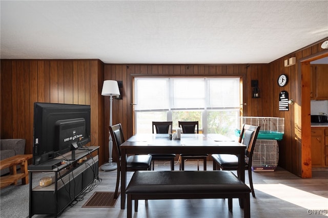 dining area featuring hardwood / wood-style flooring, wooden walls, and a textured ceiling