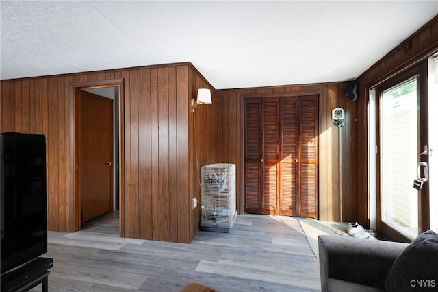 living room featuring light hardwood / wood-style flooring, wooden walls, and a textured ceiling