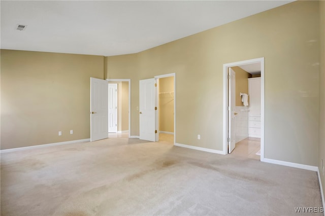 unfurnished bedroom with light colored carpet, a closet, ensuite bath, and a spacious closet