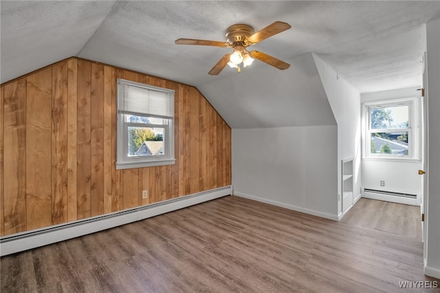 additional living space featuring wooden walls, baseboard heating, light hardwood / wood-style flooring, and a wealth of natural light