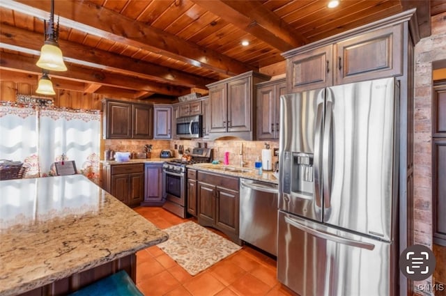 kitchen featuring light stone counters, pendant lighting, beamed ceiling, light tile patterned flooring, and appliances with stainless steel finishes