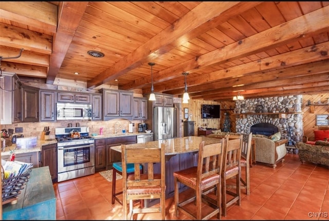 kitchen featuring pendant lighting, beamed ceiling, appliances with stainless steel finishes, and light stone countertops