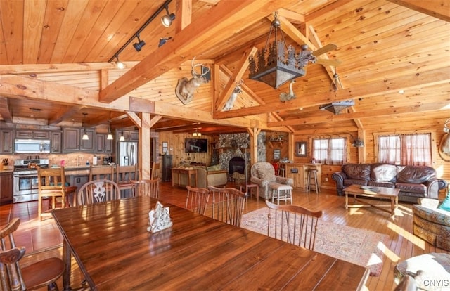 dining space with wooden ceiling, hardwood / wood-style floors, wooden walls, a stone fireplace, and track lighting