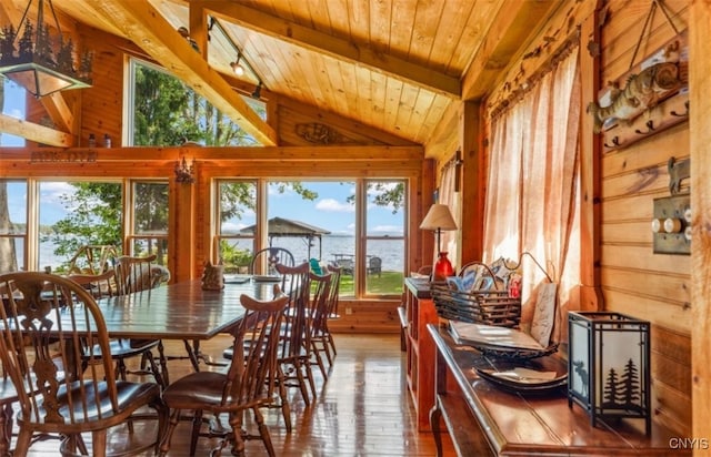 dining room with wood-type flooring, wooden walls, lofted ceiling with beams, and a water view