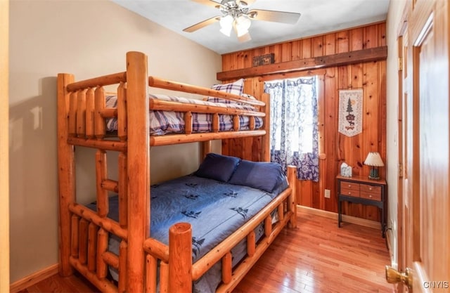 bedroom featuring ceiling fan, light wood-type flooring, and wood walls