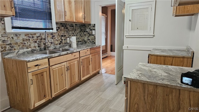 kitchen featuring light stone counters, sink, light hardwood / wood-style flooring, backsplash, and a baseboard heating unit