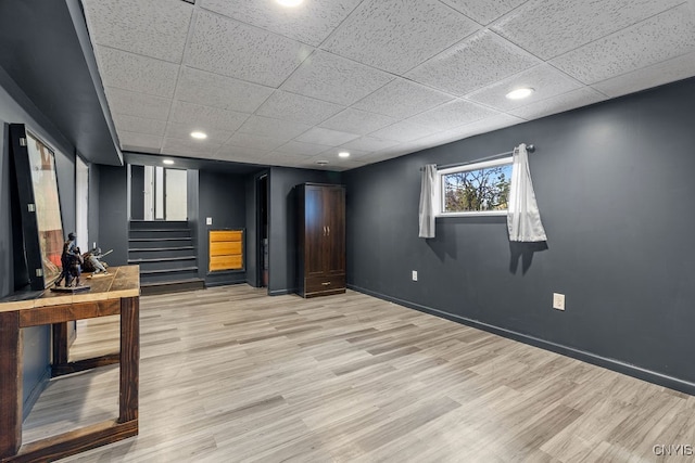 basement with light hardwood / wood-style flooring and a paneled ceiling