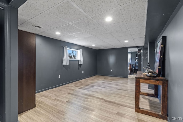 basement featuring a drop ceiling and light hardwood / wood-style floors