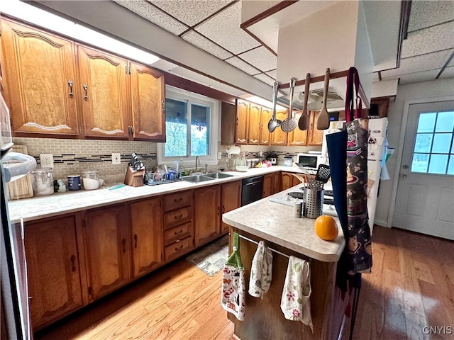 kitchen with tasteful backsplash, a paneled ceiling, sink, light hardwood / wood-style floors, and black dishwasher