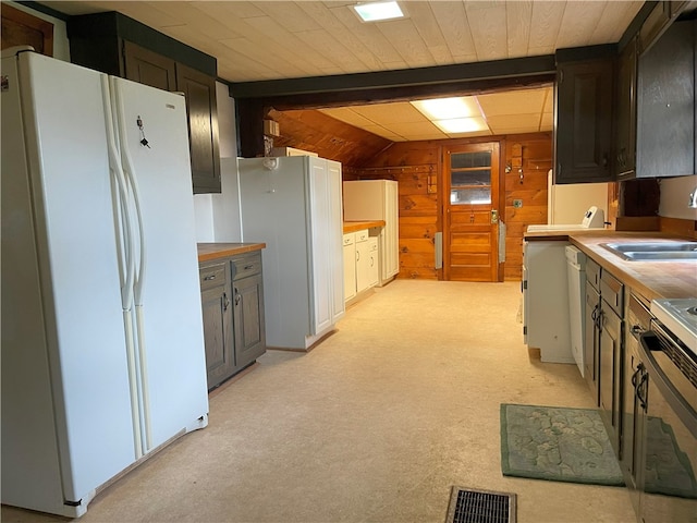 kitchen with sink, wooden counters, wood walls, white fridge, and light carpet